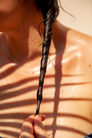 Pigtail of wet dark hair close-up. Behind the tanned bare shoulder of a woman. On the chest shadow...