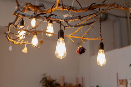 Unusual design chandelier in natural style. Several Edison retro style LED light bulbs hang on a wooden branchの写真素材