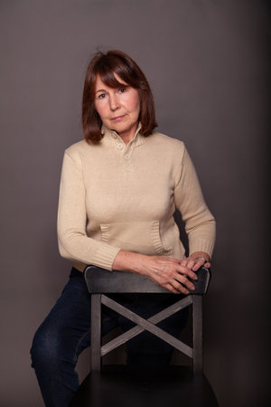 Portrait of a woman without retouching on a dark monophonic background. Elderly beautiful woman in a beige sweater looks in the frameの写真素材