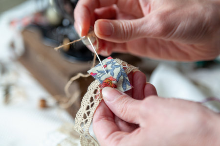 The hands of a needlewoman sew a small piece of fabric to a lace ribbon with a needle. close-upの写真素材