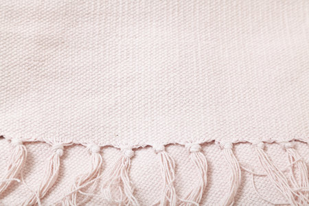 White fringe on cotton fabric. The edge of the tablecloth with fringe knots lies on a white fabric close-up. There is a place for an inscriptionの写真素材
