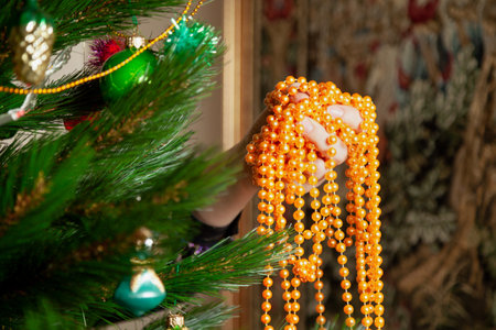 We disassemble the Christmas tree. Hands remove a yellow garland of small balls from a green spruce branch close-upの写真素材