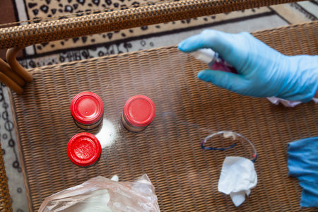 Prevention of infection at home. Hands in blue rubber gloves spray an antiseptic spray onto food jars on a glass table. close-upの写真素材