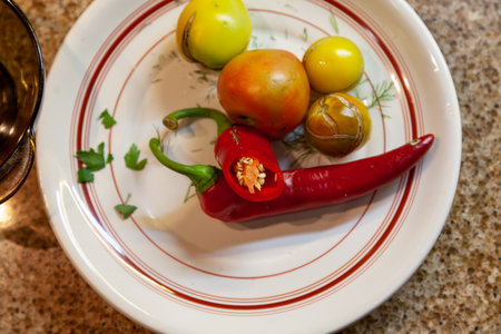 Tomatoes of varying degrees of ripeness lie on a round plate close-up. Nearby lies a pod of bitter red pepperの写真素材