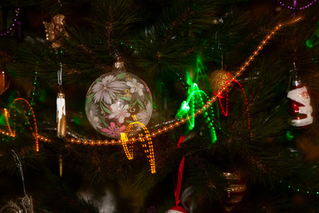 Christmas tree toy transparent ball with a floral pattern hangs on a dark background. Below is an orange garland. Around motion blur Christmas lights forms several bizarre loops.の写真素材