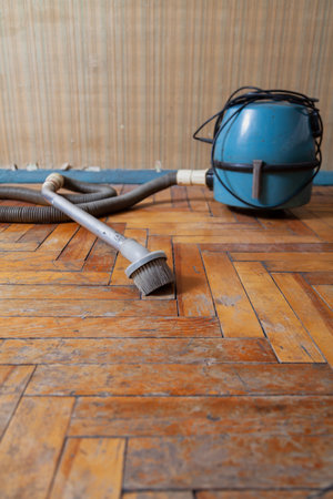 antique vacuum cleaner with a long hose stands on a scratched parquet floor in front of a wallの写真素材