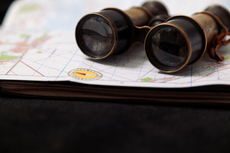 Still life with binoculars and a map. Vintage metal binoculars lie on topographic map of the area. A compass is drawn on the mapの写真素材