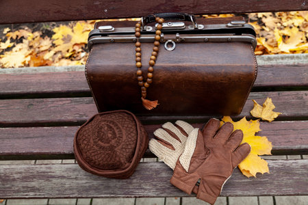 Still life with a valise and a rosary. There is a leather valise on a wooden bench in the park....