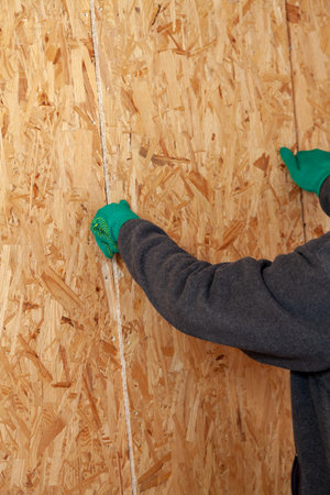 A man with a beard and green gloves installs a chipboard in a vertical structure