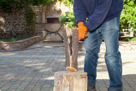 We prepare firewood for the barbecue. Hands in orange gloves chop a log on a stump with an ax on a sunny dayの写真素材