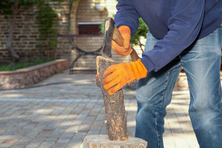 We prepare firewood for the barbecue. Hands in orange gloves chop a log on a stump with an ax on a sunny dayの写真素材