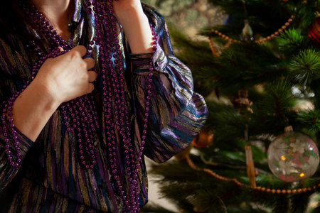 We decorate the Christmas tree. Hands hang a lilac garland of small balls on a green spruce branch close-up.の写真素材