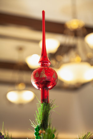 Red glass top on a Christmas tree close-up. Defocused chandelier in the backgroundの写真素材