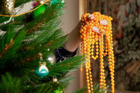 We disassemble the Christmas tree. Hands remove a yellow garland of small balls from a green spruce branch close-upの写真素材