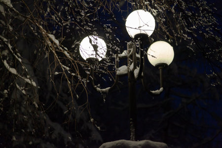 Evening street lighting. Three retro-style circular outdoor lights provide a beautiful white light. There is snow on topの写真素材
