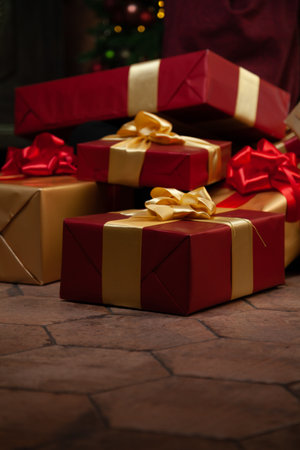 Gifts under the Christmas tree. Several boxes in beautiful packaging with red bows lie under the branches of a decorated Christmas tree.の写真素材