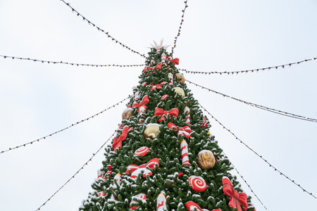 The top of the Christmas tree at the New Year fair is decorated with candies and red garlands. Light bulbs on wires radiate from the top of the treeの写真素材