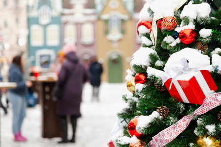 Decorated Christmas tree in the foreground at a street fair. People stand near tables against the backdrop of decorations in the style of ancient European housesの写真素材