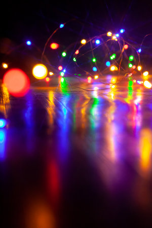 The colorful lights of an electric Christmas garland cast long, shiny paths on a smooth surface. Vertical image on a dark backgroundの写真素材