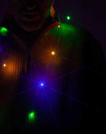 A New Year garland burns with multi-colored lights on the neck of a bearded man in a jumper with...