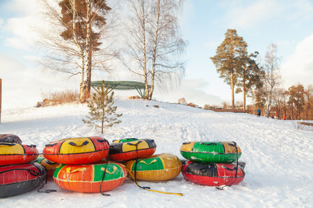 Several colored inflatable tubes lie on a mountainside in a city park on a sunny winter day. People walking in the backgroundの写真素材
