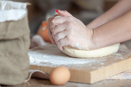 Female hands knead a piece of dough on a thick board covered with flourの写真素材