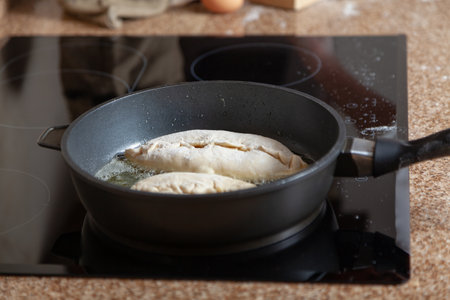 Pies are fried in a black frying pan on a black glass surface of an electric stove with a touch panel. Modern kitchenの写真素材