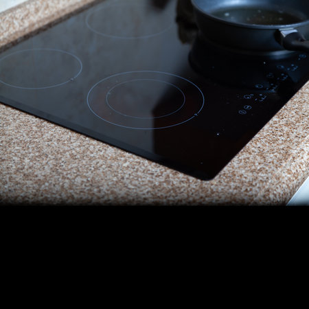 Flat built-in hob and frying pan on a marble countertop. At the bottom of the frame there is a smooth transition to a black background and a place for an inscriptionの写真素材