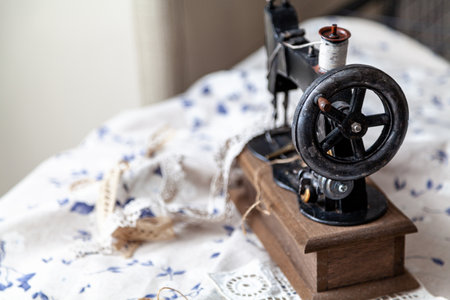 A vintage manual sewing machine stands on a white fabric with a blue pattern. Top mounted spool of white threadの写真素材