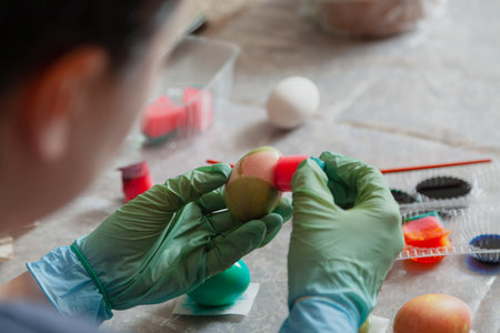 Hands with rubber blue gloves paint Easter eggs with liquid paints using a dishwashing sponge