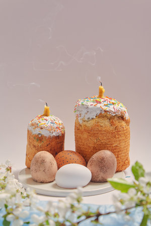 Two Easter cakes and eggs stand on a round stand on a gray background. Candles are inserted into the...