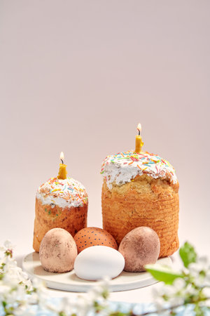 Easter still life. Two Easter cakes and eggs stand on a round stand on a white background. Burning...