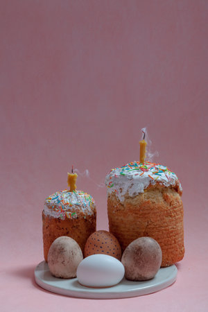 Easter still life. Two Easter cakes and eggs stand on a round stand on a pink background. Candles...