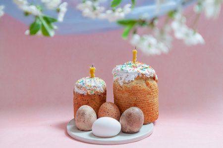 Easter still life. Two Easter cakes and eggs stand on a round stand on a pink background. Candles...