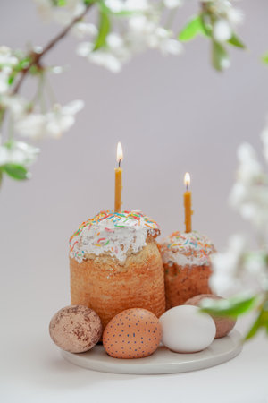 Easter still life. Two Easter cakes and eggs stand on a white background. Burning candles are...