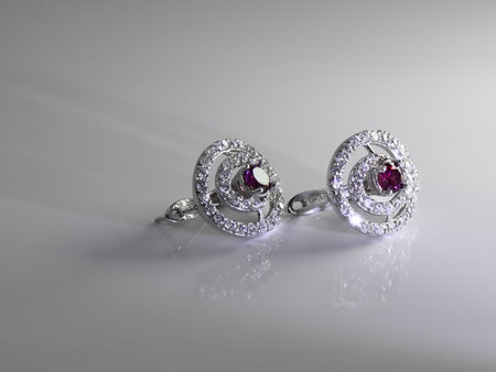 Silver jewelry accessories. Earrings with diamonds and amethyst on a light gray background shine mysteriously and reflected on the surface in a soft ray of lightの写真素材