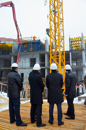 Men stand with their backs in white safety helmets on a construction site and watch the process of constructing a high-rise buildingの写真素材