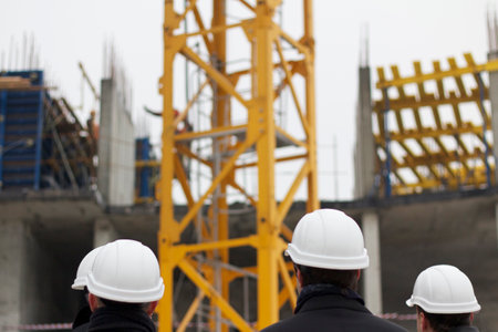 Men stand with their backs in white safety helmets on a construction site and watch the process of constructing a high-rise buildingの写真素材