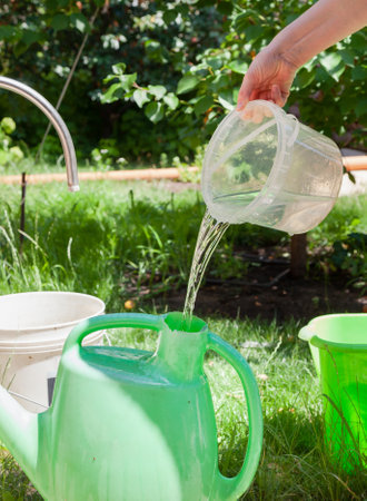 Irrigation preparation. Hands pour water into a plastic watering can for watering the garden. A jet of water pours out of a transparent plastic containerの写真素材