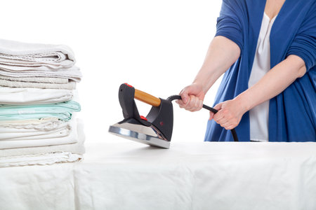 A funny scene in the laundry room. The woman hands can barely hold the iron which rushes like an angry dog onto a pile of crumpled towelsの写真素材