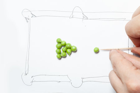 Green pea kernels in the form of a pyramid for playing billiards. The billiard table is drawn in a primitive style. Fingers imitate hitting the ball with a wooden toothpickの写真素材
