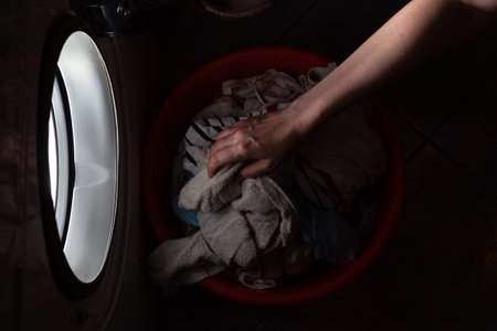 The right hand puts dirty laundry in the washing machine in a dark room. From the round hatch of the machine comes a bright lightの写真素材