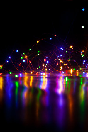 The colorful lights of an electric garland cast long, shiny paths on a smooth surface. Vertical image on a dark backgroundの写真素材