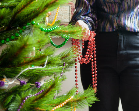 We decorate the Christmas tree. Hands hang a red garland of small balls on a green spruce branch close-upの写真素材