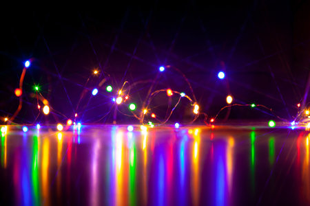 The colorful lights of an electric garland cast long, shiny paths on a smooth surface. Image on a dark backgroundの写真素材