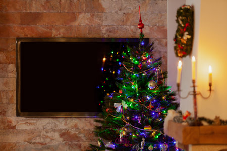 A green Christmas tree with Christmas decorations stands in the room. A large plasma TV hangs on the wall at the back.の写真素材