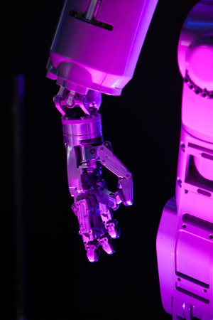 Robot body in pink light against a dark background. A mechanical hand with several fingers is clearly visible.の写真素材
