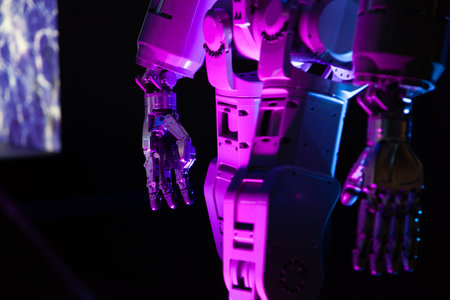 Robot body in pink light against a dark background. A mechanical hand with several fingers is...