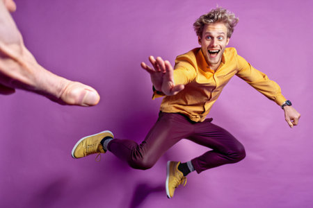 Happy young man jumping and having fun in the studio on a purple backgroundの素材