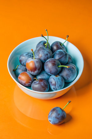 Ripe plums in a blue bowl on a bright orange backgroundの素材